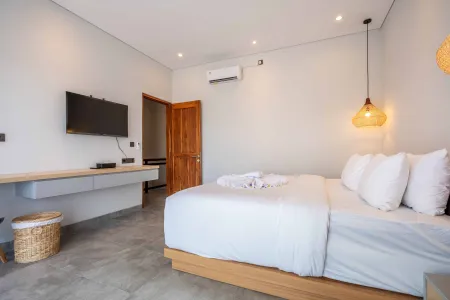 Cozy modern bedroom in a tropical villa with white linen bed, wooden accents, wall TV, and rattan lamp.
