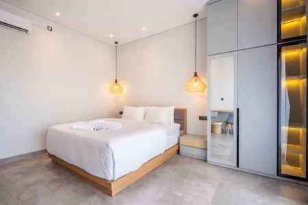 Modern minimalist bedroom featuring a white-sheeted bed, built-in gray wardrobe with LED-lit mirror, pendant lamps, and air conditioning.
