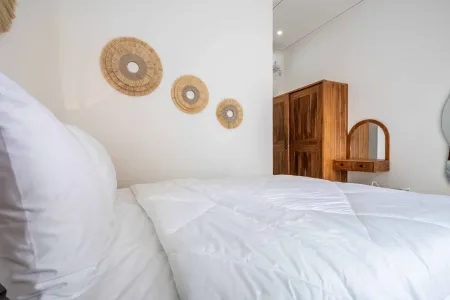 Cozy white bed in minimalist bedroom with woven rattan wall hangings and wooden wardrobe.