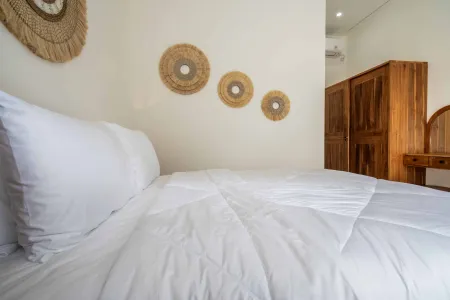 Cozy white bed in a boho-style bedroom with rattan wall hangings and wooden furniture.