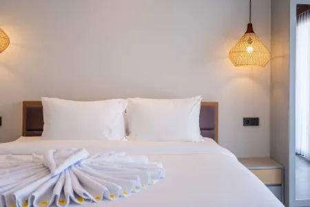 Cozy minimalist hotel bedroom with neatly made white bed, folded towels, and rattan lamps.