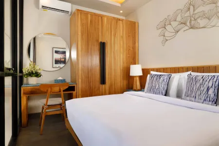 Modern tropical bedroom with white bed, blue pillows, wooden desk, wardrobe, round mirror, and decorative wall art.