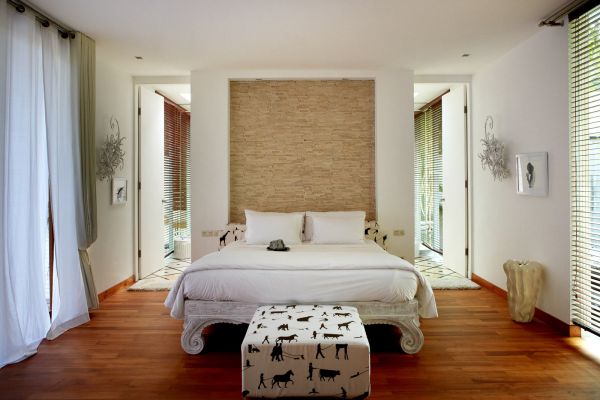 Modern luxury bedroom with white king bed, beige textured headboard, animal silhouette ottoman, and sheer-curtained windows.