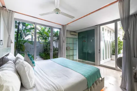 Spacious modern bedroom with king bed, sheer curtains, ceiling fan, and tropical garden views through sliding glass doors.