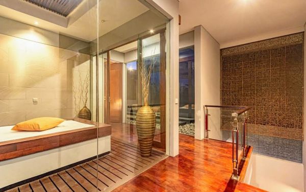 Modern tropical bedroom interior with wooden platform bed, glass sliding doors to garden, bamboo accents, and warm ambient lighting. - Bali Villas