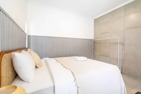 Cozy modern bedroom with rattan headboard, white duvet, pillows, and neutral concrete walls.