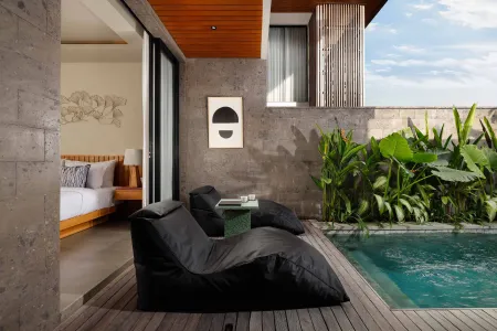 Luxurious tropical bedroom with sliding doors opening to a private infinity pool, black bean bag loungers, and lush greenery.