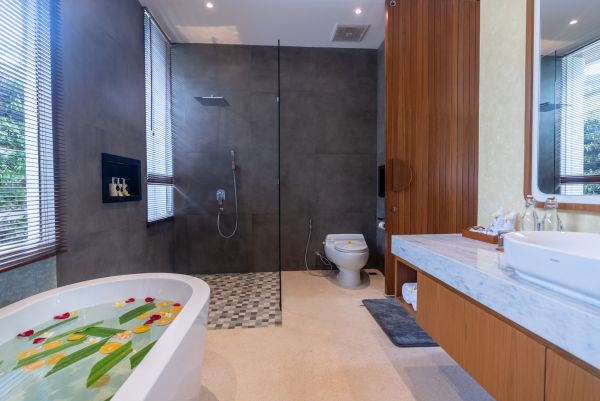 Luxurious modern bathroom featuring a freestanding bathtub with flower petals, glass shower enclosure, wooden accents, and natural light. - Bali Villas