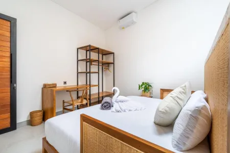 Cozy Balinese bedroom with wooden desk, rattan bed frame, white linens, and decorative swan towel.