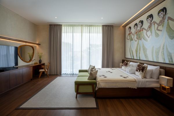 Luxurious tropical bedroom with king bed, wooden furniture, and large wall mural of Balinese dancers.