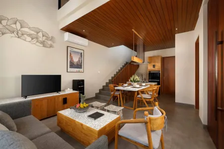 Modern open-plan living room in a Balinese villa with wooden accents, gray sofa, dining table, and integrated kitchen. - Bali Villas