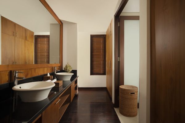 Modern luxury bathroom with double wooden vanity, white sinks on black countertop, bamboo blinds, and warm teak finishes. - Bali Villas