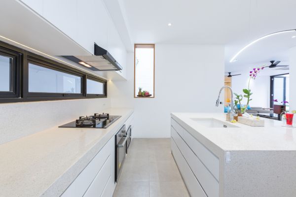 Modern white kitchen with island countertop, gas stove, stainless sink, and tropical orchid accents. - Bali Villas