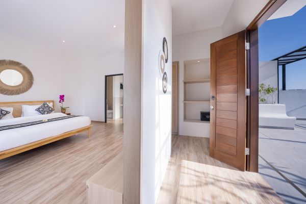 Spacious Balinese-style bedroom with king bed, woven decor, and open wooden doors to sunny balcony.
