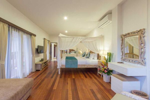 Spacious Balinese bedroom with canopy bed, wooden floors, sheer curtains, and tropical plants.