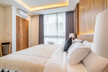 Modern wooden bedroom interior with king bed, large curtained windows, and neutral tropical decor.