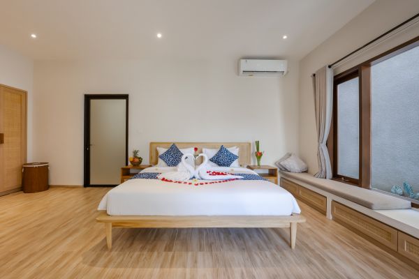 Romantic king bed adorned with rose petals and towel swans in a modern tropical bedroom with wooden floors, sheer curtains, and soft lighting.