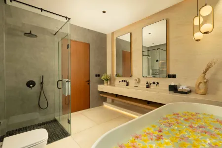 Modern luxury bathroom featuring a freestanding bathtub filled with yellow petals, glass-enclosed shower, double vanity, and tropical decor. - Bali Villas