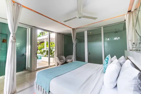 Spacious modern bedroom in a tropical villa, featuring a white king bed with teal throw, sliding glass doors to poolside garden, and ceiling fan.