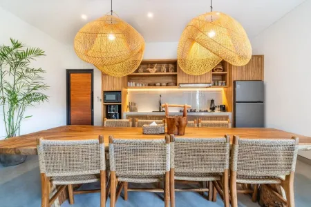 Spacious modern tropical dining room with wooden table, rattan chairs, bamboo pendant lights, and sleek kitchen cabinets. - Bali Villas