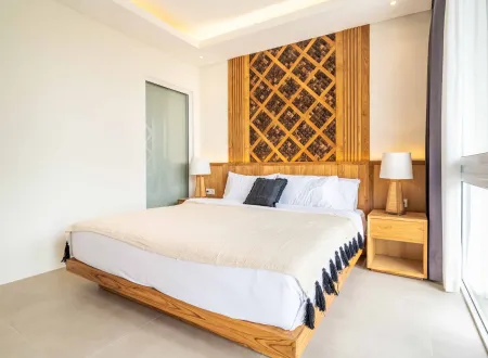 Modern minimalist bedroom with wooden lattice headboard, king bed in white linens, bedside lamps, and sliding glass doors overlooking a bright view.