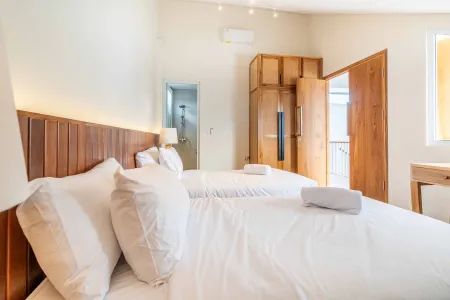 Cozy tropical bedroom with wooden headboard, white bedding, open balcony door, and built-in wardrobe.