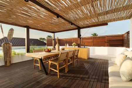 Spacious tropical rooftop terrace with wooden dining table, rattan chairs, fresh fruits, potted palms, and ocean view under bamboo pergola. - Bali Villas