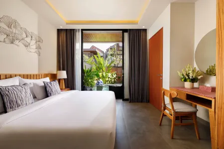 Spacious tropical bedroom with king bed, wooden accents, vanity desk, and lush garden view through sliding glass doors.