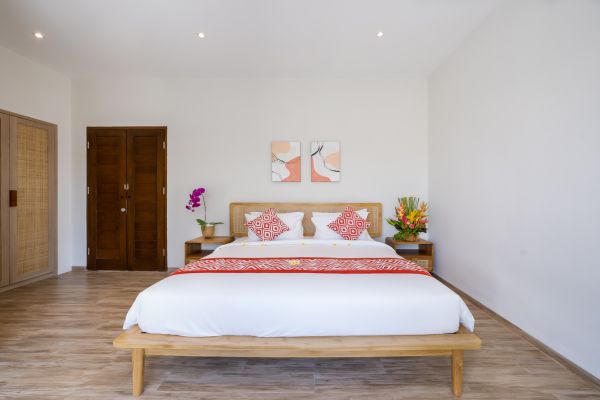 Serene Balinese bedroom with wooden platform bed, red bedding, abstract wall art, and orchids on nightstand.
