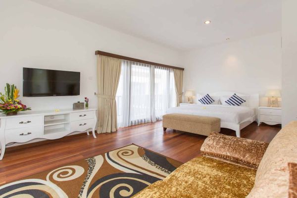 Spacious Balinese-style luxury bedroom with king bed, balcony doors, TV, and tropical decor.