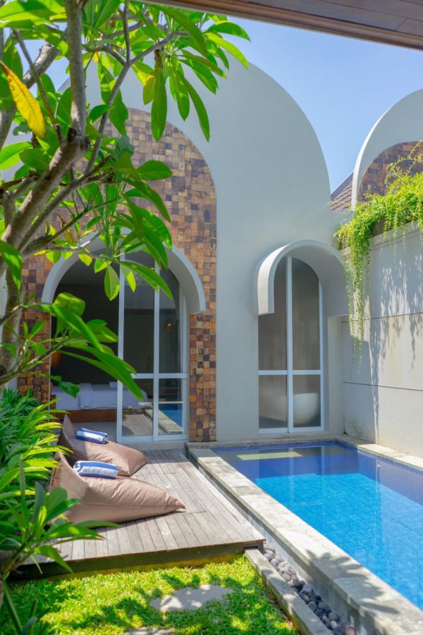 Modern tropical villa with private blue pool, arched architecture, wooden deck, and lush greenery. - Bali Villas