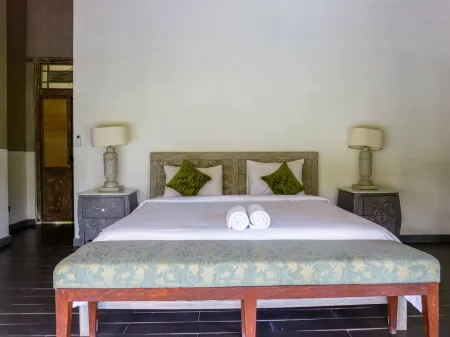 Cozy tropical bedroom with white-sheeted king bed, green accent pillows, bedside lamps, and wooden bench.