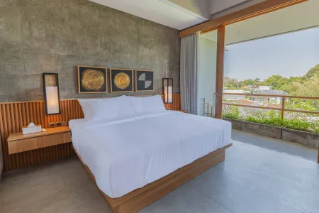 Spacious modern bedroom with a king-sized bed, wooden accents, abstract circular wall art, bedside lamps, and sliding doors opening to a lush tropical balcony view.