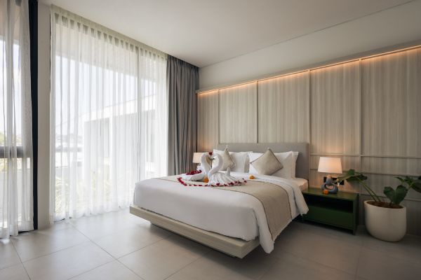 Luxurious hotel bedroom with king bed decorated in rose petals and towel swans, sheer curtains, potted plants, and garden views. - Bali Villas