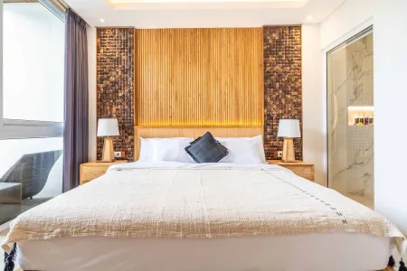 Modern bedroom with king-sized bed, wooden slat headboard, bedside lamps, purple curtains, and adjacent frosted glass door.