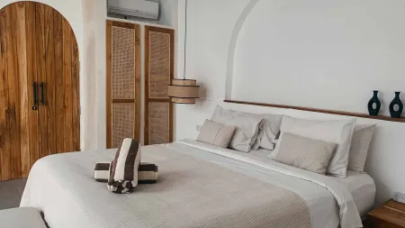 Serene tropical bedroom with king-size bed in white linens, wooden arched headboard, rattan screens, pendant lamp, and minimalist decor.