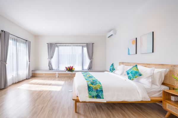 Spacious tropical bedroom with a wooden king bed, teal accents, large curtained windows, and abstract wall art.