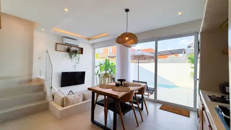 Modern tropical villa interior with wooden dining table, rattan pendant light, plants, and sliding doors to private pool. - Bali Villas