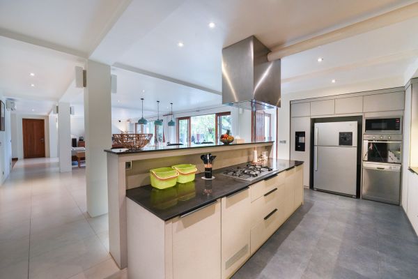 Modern open-plan kitchen with white cabinets, black granite island, stainless steel appliances, and tropical wood accents. - Bali Villas