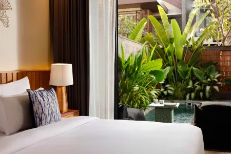 Luxurious tropical bedroom with king bed, open sliding doors to lush green garden and private plunge pool.