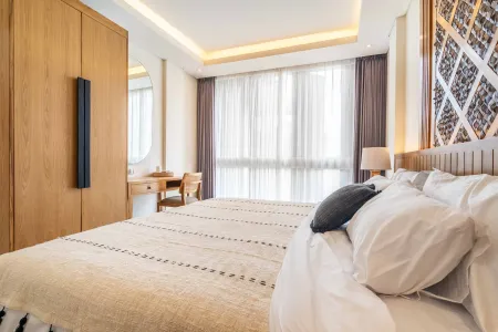 Modern bedroom interior with wooden wardrobe, king bed with white linens, desk, and large sheer-curtained windows.