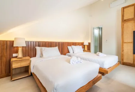 Cozy tropical bedroom with two wooden platform beds, white linens, folded towels, and bedside lamps.