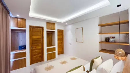 Modern tropical bedroom with wooden cabinets, king bed in green floral bedding, floating shelves, and warm LED lighting.