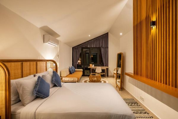 Cozy tropical bedroom interior with rattan headboard bed, orange sofa, wooden slat walls, and night-view window.
