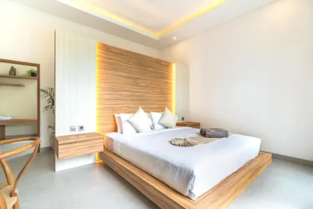 Modern bedroom with wooden platform bed, white linens, illuminated oak headboard, desk, and plants.