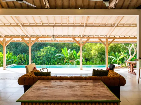 Open-air Balinese pavilion with tufted beige sofas and wooden table, overlooking turquoise infinity pool and lush tropical jungle. - Bali Villas