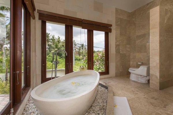 Luxurious Balinese bathroom with freestanding stone bathtub, tropical garden view, and floating frangipani petals. - Bali Villas
