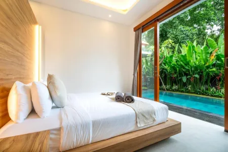 Luxurious tropical bedroom with wooden platform bed, white linens, and sliding doors opening to lush garden and infinity pool.