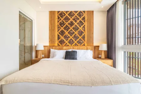 Cozy modern bedroom featuring a king-size bed with wooden lattice headboard, white linens, bedside lamps, and floor-to-ceiling windows with sheer curtains.