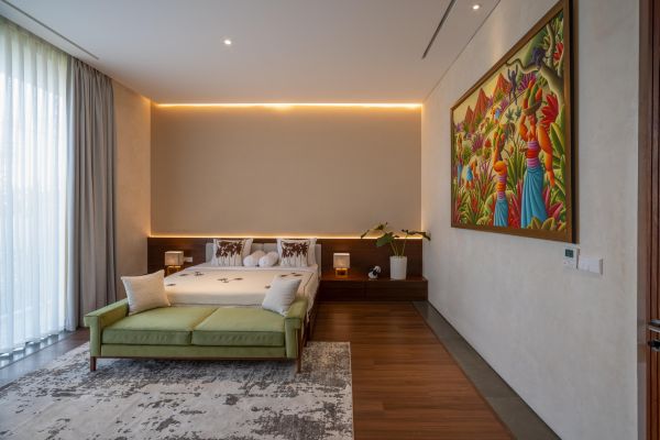 Modern bedroom with king bed, green velvet daybed, vibrant folk art painting, sheer-curtained windows, and warm wooden floors.